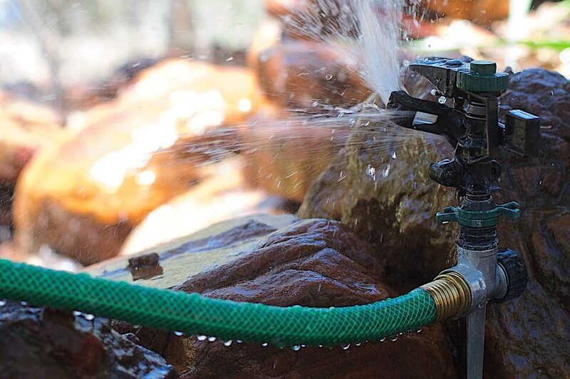 Garden sprinkler head spraying water over rocks and garden plants