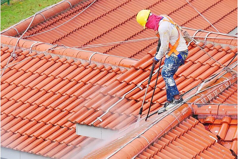 Worker pressure-washing a tiled residential roof