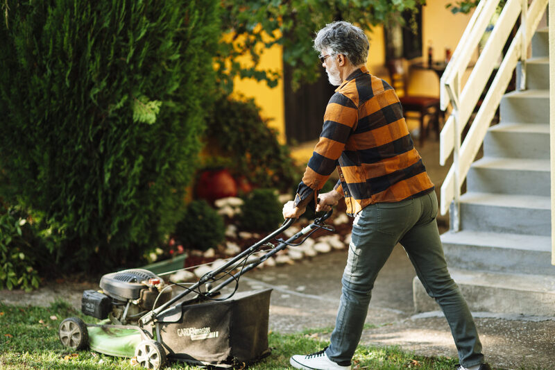Gardener mowing a suburban Christchurch lawn with a petrol lawnmower